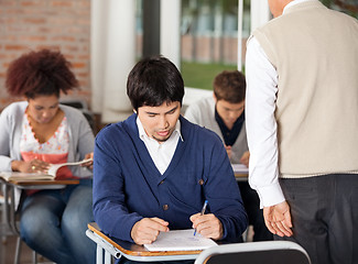 Image showing Students Giving Exam While Teacher Supervising Them In Classroom