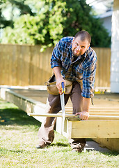 Image showing Mid Adult Worker Cutting Wood With Saw At Construction Site