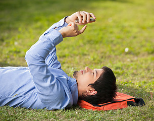 Image showing Man Using Mobilephone While Lying On Grass At Campus