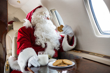 Image showing Santa Holding Cookie While Looking Through Private Jet's Window