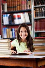 Image showing Happy Schoolgirl Sitting With Stack Of Books In Library