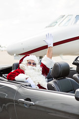 Image showing Santa Waving Hand In Convertible Against Private Jet