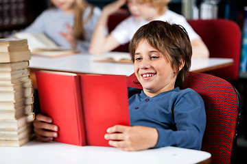 Image showing Schoolboy Smiling While Reading Book At Table In Library