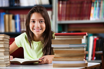 Image showing Schoolgirl Smiling While Sitting With Stack Of Books In Library
