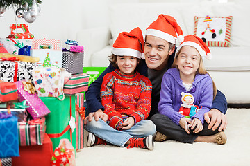 Image showing Father And Siblings Sitting By Stacked Christmas Presents