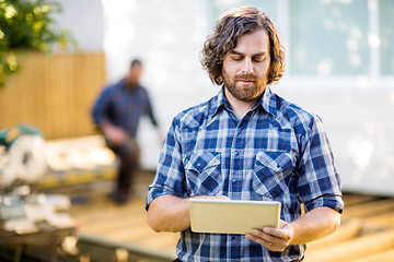 Image showing Carpenter Using Digital Tablet With Coworker Working In Backgrou