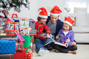 Image showing Siblings And Father Reading Book By Christmas Presents