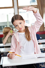 Image showing Schoolgirl Raising Hand At Desk In Classroom