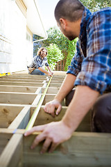 Image showing Carpenter Measuring Wood With Tape While Looking At Coworker