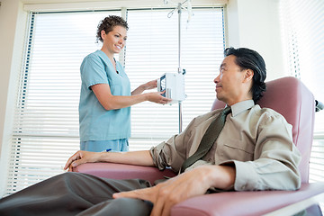 Image showing Nurse Looking At Patient While Adjusting IV Machine