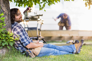 Image showing Relaxed Carpenter Holding Disposable Cup While Leaning On Tree T