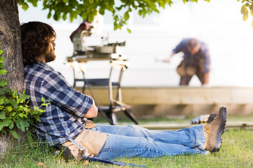 Image showing Construction Worker Leaning On Tree Trunk