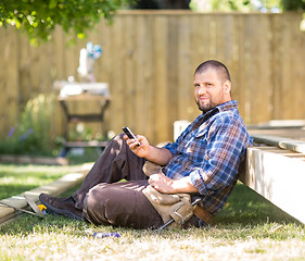 Image showing Confident Carpenter Messaging On Cellphone While Leaning On Wood