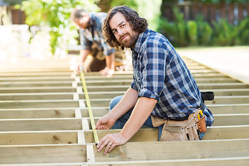 Image showing Carpenter Measuring Wood With Tape While Coworker Assisting Him