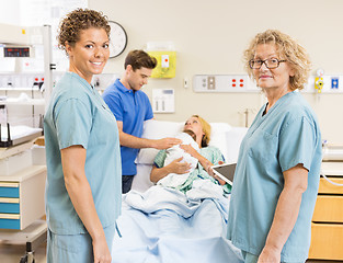 Image showing Smiling Nurses Standing Against Couple With Baby In Background