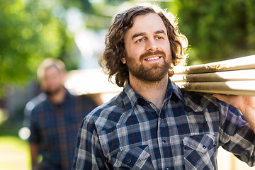 Image showing Carpenter Smiling While Carrying Planks With The Help Of Coworke