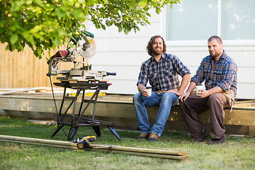 Image showing Carpenters Holding Disposable Cups While Sitting On Wooden Frame