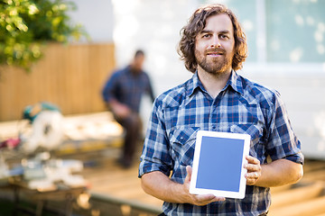 Image showing Carpenter Displaying Tablet Computer With Coworker Working In Ba