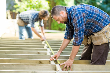 Image showing Carpenters Measuring Wood With Tape At Construction Site