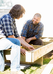 Image showing Worker Looking At Coworker Measuring Wood At Site