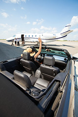 Image showing Woman In Convertible Waving To Pilot And Stewardess Against Jet