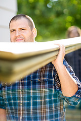 Image showing Carpenter Carrying Wooden Planks Outdoors