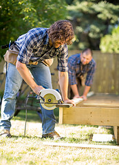 Image showing Carpenter Cutting Wood With Handheld Saw While Coworker Assistin