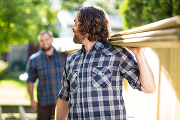 Image showing Carpenter And Coworker Carrying Wooden Planks