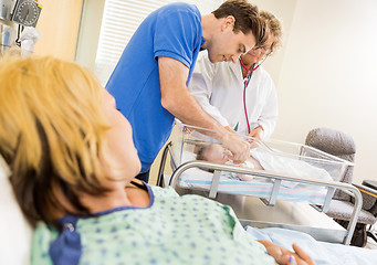 Image showing Mature Doctor Examining Newborn Babygirl While Couple Looking At
