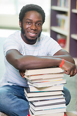 Image showing Smiling Student With Stacked Books Sitting In Library