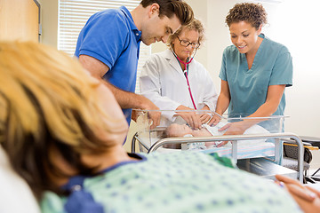 Image showing Doctor Examining Baby By Nurse And Man With Mother In Foreground