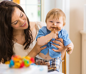 Image showing Mother Holding Baby Boy Eating Cake With Icing On Face