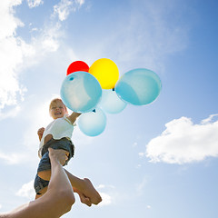 Image showing Mother Lifting Daughter Holding Balloons Against Cloudy Sky