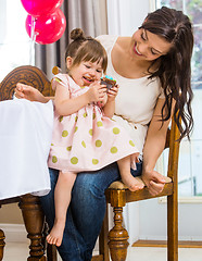 Image showing Girl Eating Cupcake While Sitting On Mother's Lap