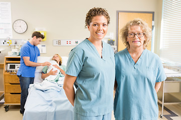 Image showing Confident Nurses Standing Against Couple With Baby In Background