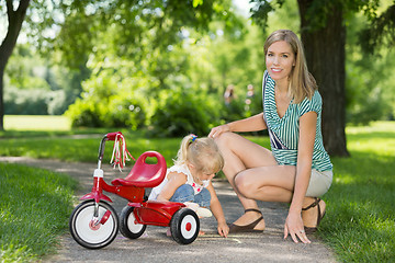 Image showing Mother With Daughter Crouching By Tricycle On Walkway