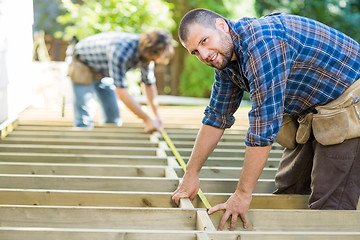 Image showing Carpenter Measuring Wood With Tape While Coworker Assisting Him