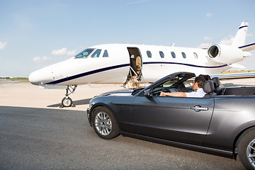 Image showing Pilot In Convertible Parked Against Private Jet