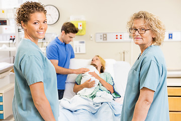 Image showing Successful Nurses Standing Against Couple With Baby In Backgroun