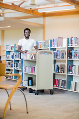 Image showing Librarian With Trolley Of Books Smiling In Bookstore