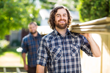 Image showing Happy Carpenter With Coworker Carrying Planks Outdoors