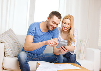 Image showing smiling couple with papers and calculator at home