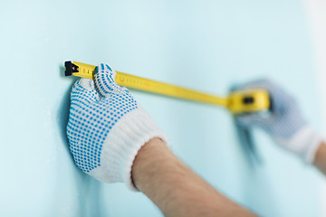 Image showing closeup of male in gloves measuring wall with tape