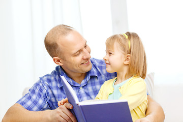 Image showing smiling father and daughter with book at home