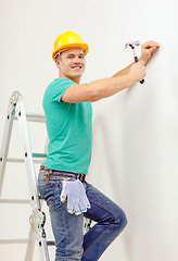 Image showing smiling man in helmet hammering nail in wall