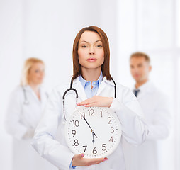 Image showing calm female doctor with wall clock