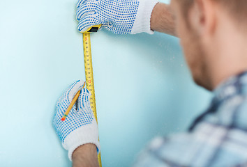 Image showing closeup of male in gloves measuring wall with tape