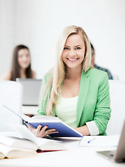 Image showing smiling young woman reading book at school