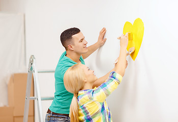 Image showing smiling couple painting small heart on wall