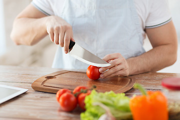 Image showing male hand cutting tomato on board with knife